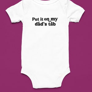 Pode incluir: Um macacão branco para bebê com texto preto que diz "Put it on my dad's tab".