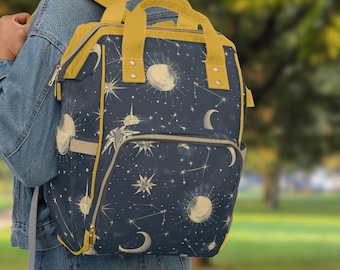 Puede incluir: Una mochila azul marino con un estampado celestial con lunas, estrellas y constelaciones. La mochila tiene correas y ribetes amarillos.