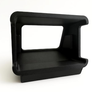 Pu&ograve; includere: Un oggetto nero rettangolare stampato in 3D con una superficie strutturata. Presenta un ampio spazio rettangolare aperto al centro, con una base a forma di mensola. L'oggetto ha angoli arrotondati e un design angolare robusto.