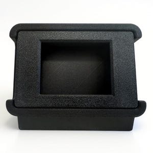May include: A black, rectangular, 3D-printed object with a textured surface. It features a recessed square opening in the center and rounded edges. The object is designed to hold or display a small item.