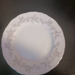 Puede incluir: Un plato de cerámica blanco con un borde plateado y un delicado diseño floral en gris.