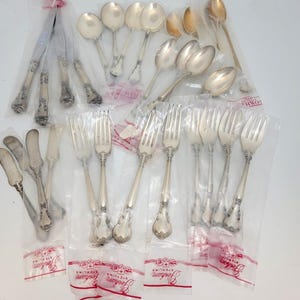 May include: A selection of Gorham Sterling silverware, including forks, spoons, and knives, packaged in clear plastic bags. The silverware has ornate, detailed handles and a shiny, silver finish. The bags have a red and white label.