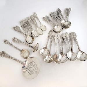 May include: A collection of ornate silver serving spoons and ladles. The spoons have detailed floral designs on the handles and bowls. The set includes various sizes and shapes, perfect for serving a variety of dishes.