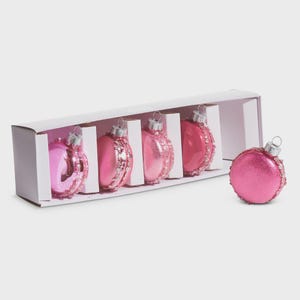 May include: A set of six pink Christmas ornaments in a white box. Five ornaments are arranged inside the box, and one is displayed separately. The ornaments have a shiny, glittery finish and are decorated with silver accents.