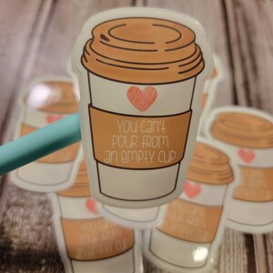 May include: A sticker featuring a coffee cup design with a brown lid and a heart. The cup has a brown sleeve with the text "You can't pour from an empty cup". Several similar stickers are visible in the background.