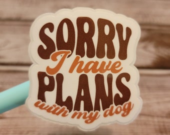 May include: A white sticker with the text "SORRY I have PLANS with my dog" in brown and orange retro font. The sticker has a white border and is likely for use on a laptop, water bottle, or other personal items.