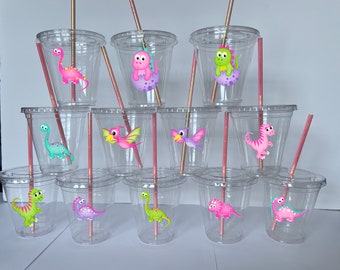 May include: Set of 12 clear plastic cups with dinosaur themed designs. Each cup has a pink, green, or blue dinosaur with a pink straw.
