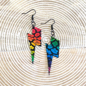 May include: A pair of rainbow lightning bolt earrings with a black leopard print pattern. The earrings have black hooks.