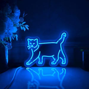 Pode incluir: Uma placa de néon azul em forma de gato andando. A placa está acesa e projeta um brilho azul na superfície em que está sentada.