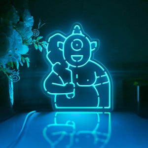 Op de afbeelding: Een blauwe neonlamp in de vorm van een eenogig monster met een grote glimlach. Het monster houdt een groot voorwerp vast in zijn rechterhand.