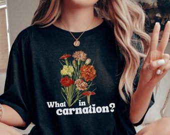 Peut inclure: T-shirt noir avec un motif floral et le texte "What in carnation?" imprimé sur le devant.