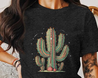 以下が含まれることがあります： 鮮やかなサボテンのイラストが描かれた濃いグレーのTシャツ。デザインは、ピンク、緑、オレンジの色合いでアクセントをつけた、複数の腕を持つ中央のサボテンが特徴です。小さなサボテンと星が、砂漠をテーマにしたグラフィックを完成させています。