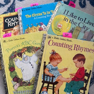 Puede incluir: Una colección de libros Little Golden Book vintage con ilustraciones coloridas. Los títulos incluyen "The Circus Is in Town", "I Like to Live in the City" y "Counting Rhymes". Los libros tienen notas adhesivas rosas con números.