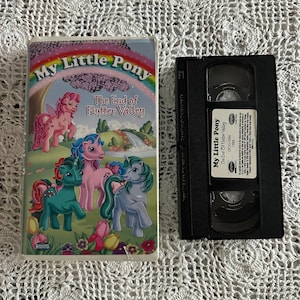 Op de afbeelding: Een vintage VHS-band en de hoes voor "My Little Pony: The End of Flutter Valley". De hoes bevat kleurrijke illustraties van de pony's, een regenboog en de titeltekst. De VHS-band is zwart met een wit label.
