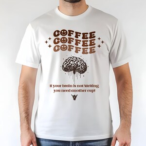 May include: White t-shirt with a brown coffee-themed design. The design includes the word "COFFEE" repeated three times with smiley faces, a brain graphic, and the text "If your brain is not Melting you need another cup!"