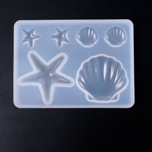 Könnte beinhalten: Transparente Silikonform mit fünf Vertiefungen zum Herstellen von Kunsthandwerk aus Harz. Die Form verfügt über zwei kleine Sternfischformen, zwei kleine Muschelformen und eine große Muschelform.