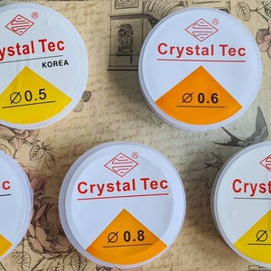 Könnte beinhalten: Fünf weiße Behälter mit gelben Deckeln und rotem Text. Die Behälter sind mit "Crystal Tec" beschriftet und haben unterschiedliche Größen: 0,5, 0,6, 0,7, 0,8 und 1,0.