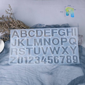 Könnte beinhalten: Eine transparente Silikonform zum Herstellen von Buchstaben und Zahlen aus Harz. Die Form ist 19,4 cm x 36 cm groß und enthält das Alphabet und die Zahlen 0-9.