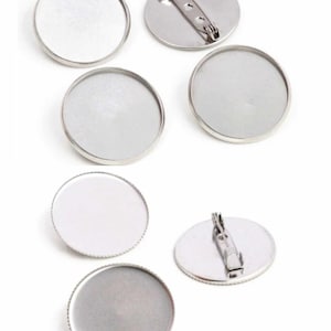 Könnte beinhalten: Sechs runde, silberfarbene Metall-Cabochon-Fassungen mit Sicherheitsnadel. Die Fassungen sind für die Herstellung von individuellen Schmuckstücken geeignet.