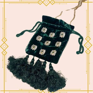 Pode incluir: Uma bolsa de cordão de veludo verde escuro com uma alça de corrente e várias borlas. A bolsa é decorada com strass brilhantes em um padrão geométrico.