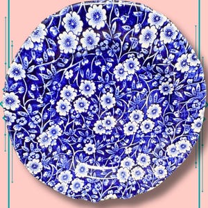 May include: A round, blue and white ceramic plate with a floral pattern. The plate features a repeating design of white flowers and leaves against a dark blue background. The plate is a decorative item.