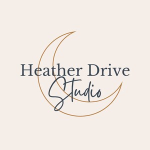 May include: A logo design featuring the text "Heather Drive Studio" in a dark blue serif font, with "Studio" in a cursive script. A gold crescent moon shape frames the text on a cream background.