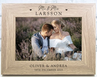 May include: A wooden picture frame with a photo of a couple in a field of flowers. The frame is engraved with "Mr. & Mrs. LARSSON" and "OLIVER & ANDREA 14TH DECEMBER 2023".
