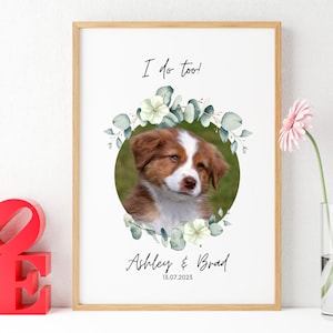May include: A framed print with a white background and a photo of a brown and white puppy in a circle surrounded by a green floral wreath. The text "I do too!" is above the photo and "Ashley & Brad 15.07.2023" is below the photo.
