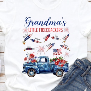 Puede incluir: Camiseta blanca con un diseño de camión rojo, blanco y azul y fuegos artificiales. El texto "Grandma's Little Firecrackers" está impreso en la camiseta. El camión tiene los nombres de los niños impresos en los fuegos artificiales.