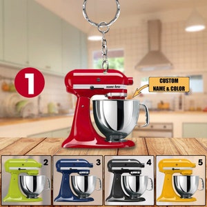 May include: A red miniature kitchen stand mixer keychain with a silver mixing bowl. The keychain has a silver ring and chain. The image also shows four other stand mixer keychains in green, blue, black, and yellow. Text on the image says "CUSTOM NAME & COLOR".