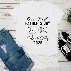 May include: White t-shirt with black text that reads "Our First Father's Day Ctrl + C Evelyn & Daddy 2025".