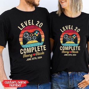 May include: Two black t-shirts with a retro video game controller graphic and the text "Level 20 Complete" with names and a date. The text reads "Level 20 Complete Henry Nicole June 20th, 2004".