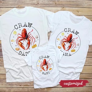 May include: Three white t-shirts with a crawfish design and the words "Craw Dad", "Craw Ima", and "Craw Baby".