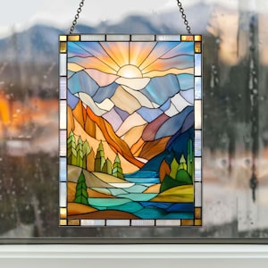 May include: Stained glass panel depicting a mountain landscape with a setting sun. The artwork features a vibrant color palette of blues, oranges, and greens, with a chain for hanging. The panel is rectangular and framed.