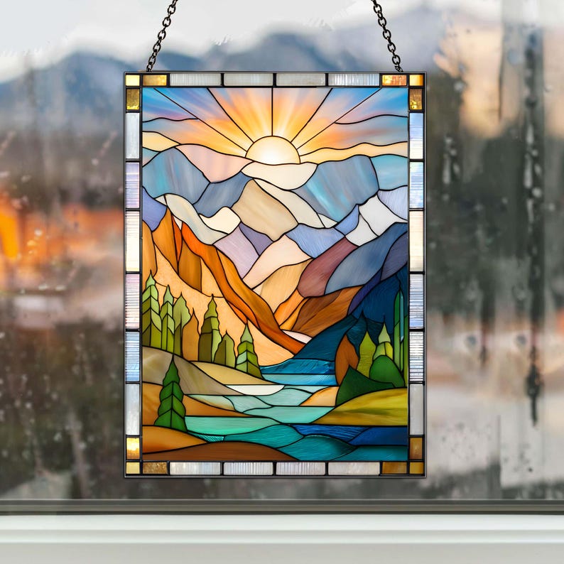 May include: Stained glass panel depicting a mountain landscape with a setting sun. The artwork features a vibrant color palette of blues, oranges, and greens, with a chain for hanging. The panel is rectangular and framed.