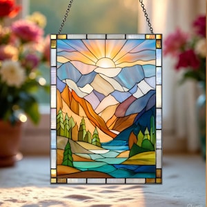 May include: A rectangular stained glass panel depicting a mountain landscape with a setting sun. The artwork features a vibrant color palette of blues, oranges, greens, and yellows, with a chain for hanging. The design includes mountains, trees, and a river.