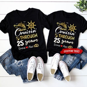 Op de afbeelding: Twee zwarte T-shirts met een gouden schip-, anker- en stuurwielontwerp. De tekst op de shirts luidt "Cruisin' Through 25 years". De shirts zijn gepersonaliseerd met de namen "Emma" en "Alex".