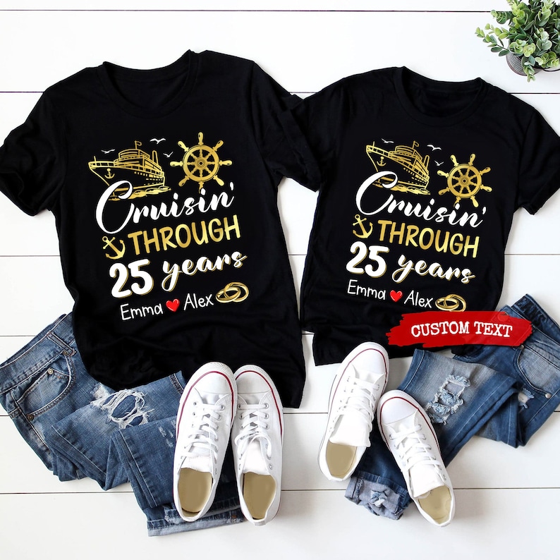 Op de afbeelding: Twee zwarte T-shirts met een gouden schip-, anker- en stuurwielontwerp. De tekst op de shirts luidt "Cruisin' Through 25 years". De shirts zijn gepersonaliseerd met de namen "Emma" en "Alex".