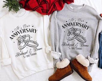 Puede incluir: Dos sudaderas blancas y grises con el texto "It's Our Anniversary" y un diseño de anillo. El texto también incluye los nombres "Richard & Diane" y la fecha "5/20/1990".