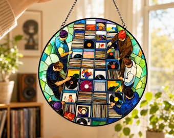 May include: A circular stained glass suncatcher featuring a detailed scene of people browsing through rows of vinyl records in crates. The artwork uses vibrant blue, green, and multi-colored glass segments to depict the figures and record sleeves.