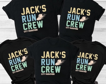 Może przedstawiać: Czarne koszulki z napisem "JACK'S RUN CREW CITY MARATHON" i grafiką buta do biegania. Koszulki z krótkim rękawem są odpowiednie na imprezy biegowe i maratony.