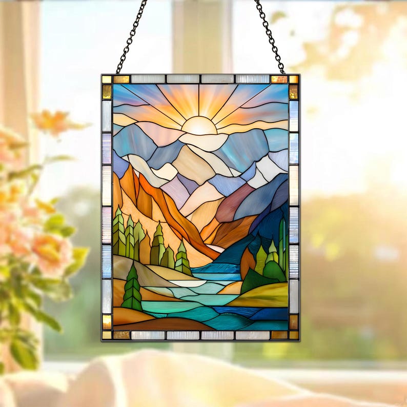 May include: Stained glass panel depicting a mountain landscape with a sunrise. The artwork features a vibrant color palette of blues, oranges, and greens, with a chain for hanging. The design includes mountains, trees, and a river.