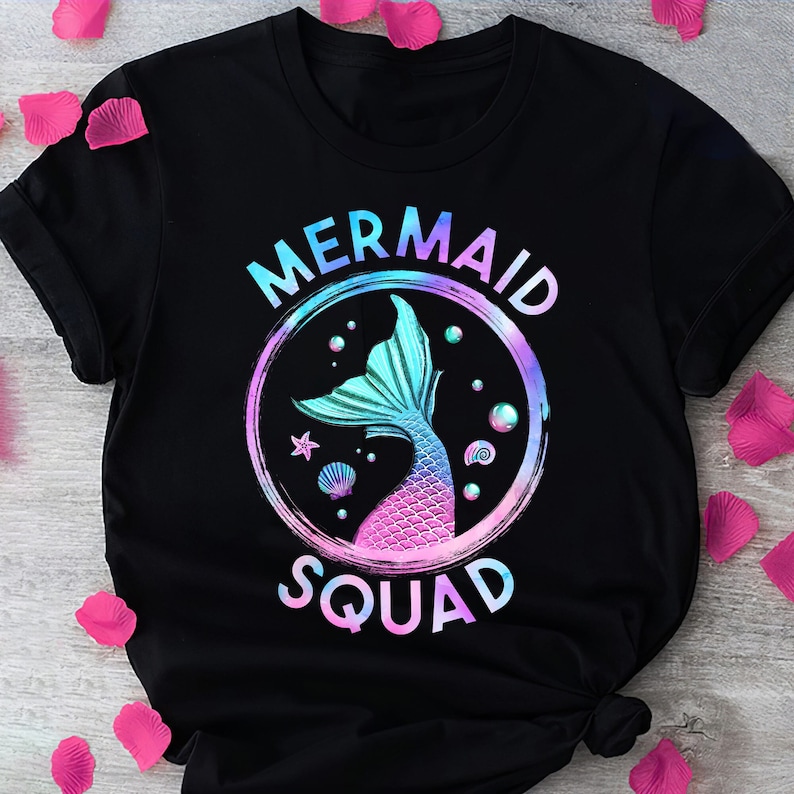 Pu&ograve; includere: Maglietta nera con una grafica di coda di sirena e il testo "Mermaid Squad" in un gradiente arcobaleno.
