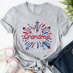 May include: Gray t-shirt with a red, white, and blue firework design. The fireworks are labeled with the names "Chad", "Ruby", "Olivia", "Benten", and "Jasmine". The text "Grandma" is in the center of the design.