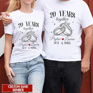 Peut inclure: Deux t-shirts blancs avec un graphique de deux anneaux entrelacés avec un diamant au sommet. Le texte sur les t-shirts est "20 ANS ensemble Peyton Lauren OCT 4, 2005".