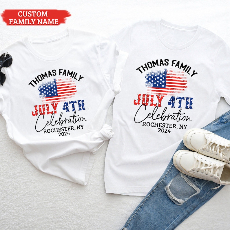 K&ouml;nnte beinhalten: Zwei wei&szlig;e T-Shirts mit einem verwitterten amerikanischen Flaggen-Design und dem Text "Thomas Family July 4th Celebration Rochester, NY 2024".