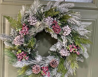 May include: A festive Christmas wreath with frosted pine needles, pinecones, and red berries. The wreath is a circular design, perfect for holiday decor. The wreath is displayed on a green door.