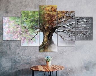 May include: A five-piece canvas print set depicting a tree in four different seasons. The tree is painted in shades of pink, green, yellow, brown, and white. The background is a gray wall with a wooden table and two stools.