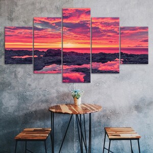Op de afbeelding: Een vijfdelige canvas print set die een levendige zonsondergang over een rotsachtige kustlijn toont. De lucht is een mix van roze, oranje en paarse tinten, met wolken die in het water worden weerspiegeld.