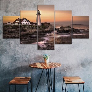 Puede incluir: Impresión en lienzo de cinco paneles que representa un faro al atardecer. El faro blanco se alza junto a un edificio blanco con tejado rojo, situado en una costa rocosa. El cielo transita del naranja al morado.